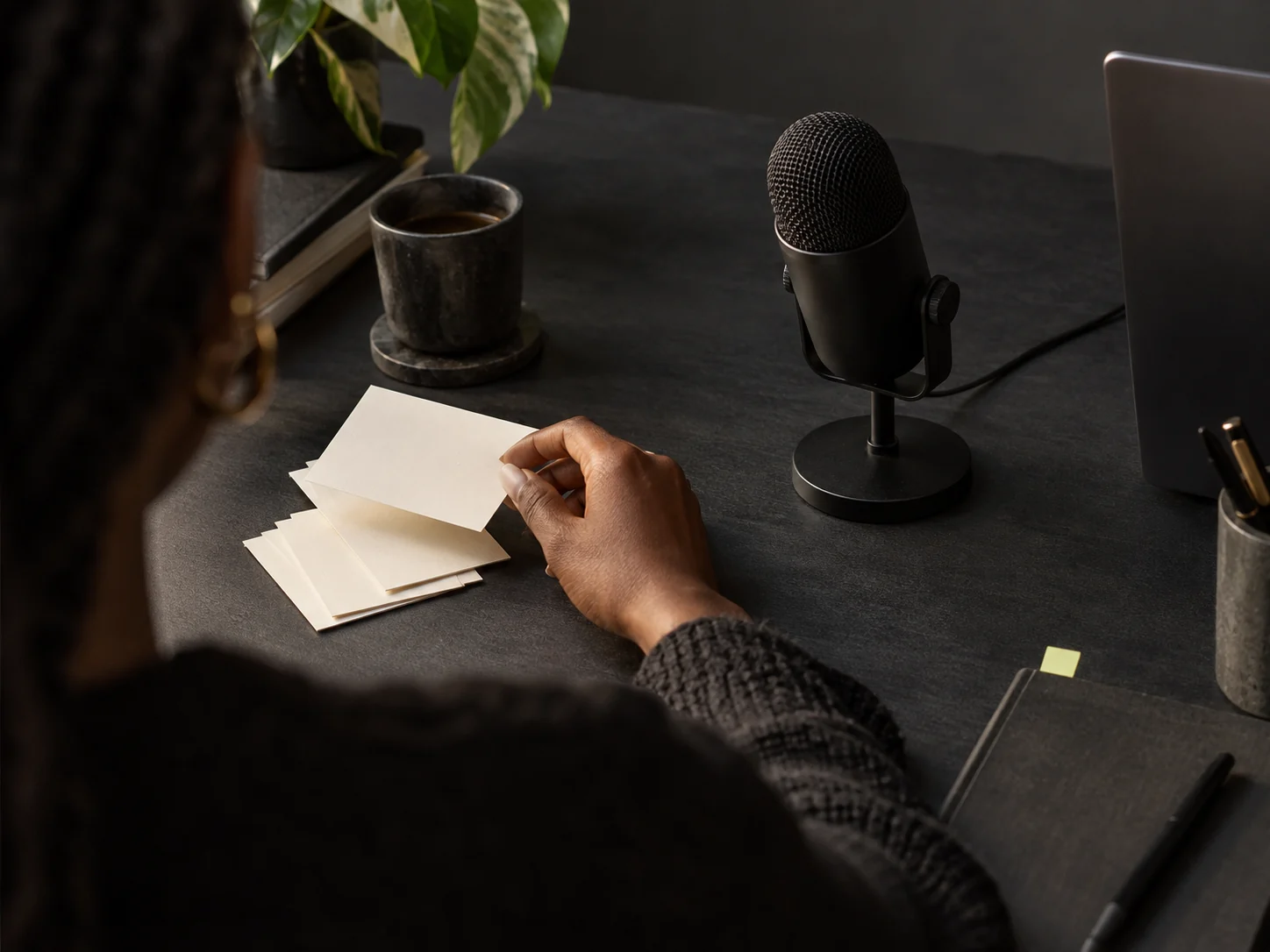 Illustrative detail of a creator arranging blank note cards beside a microphone.